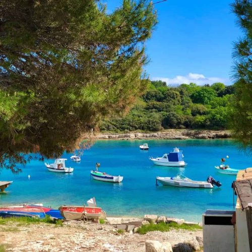 A peaceful coastal bay with anchored boats, turquoise water, and lush greenery in the background.