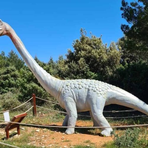 A life-sized dinosaur model of a Brachiosaurus on display in Dinopark surrounded by greenery.
