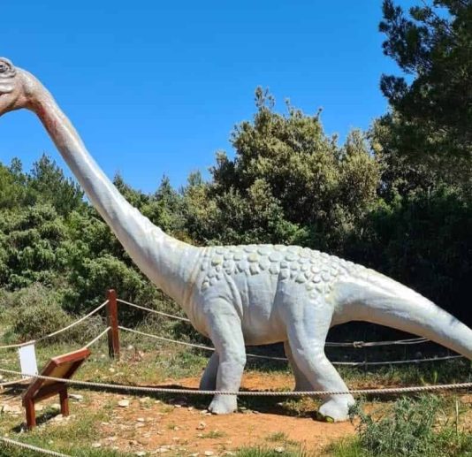 A life-sized dinosaur model of a Brachiosaurus on display in Dinopark surrounded by greenery.